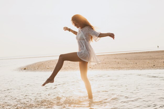 Joven mujer hermosa delgada en la playa al atardecer