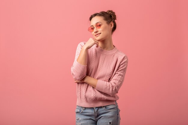 Joven mujer hermosa muy sonriente en elegante traje de primavera con suéter rosa y gafas de sol aisladas sobre fondo rosa de estudio