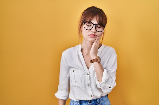 Joven mujer hermosa con pantalones casual sobre fondo amarillo tocando la boca con la mano con expresión dolorosa debido a dolor de muelas o enfermedad dental en los dientes. dentista