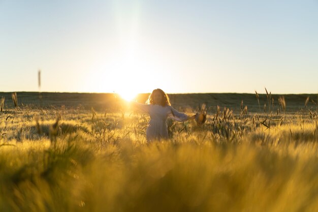 joven mujer hermosa con el pelo largo y rubio con un vestido blanco en un campo de trigo temprano en la mañana al amanecer. El verano es el momento de los soñadores, el pelo volador, una mujer corriendo por el campo bajo los rayos.