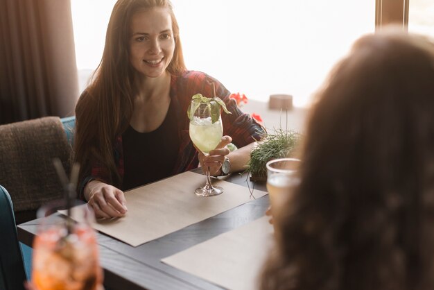 Joven mujer hermosa sentada con sus amigos sosteniendo bebidas