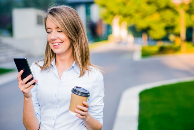 Joven mujer inteligente de lectura profesional con teléfono. Mujer de negocios de lectura de noticias o mensajes de texto sms en smartphone, mientras que el consumo de café en el descanso del trabajo.