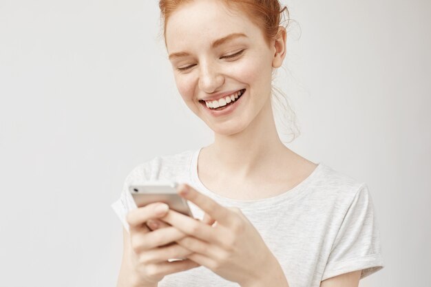 Joven mujer de jengibre sonriendo, enviando mensajes de texto publicando fotos en las redes sociales con una sonrisa