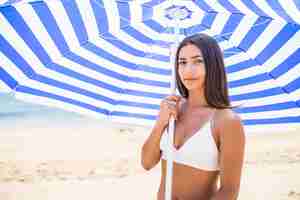 Foto gratuita joven mujer latina vistiendo bikini bajo una sombrilla de playa