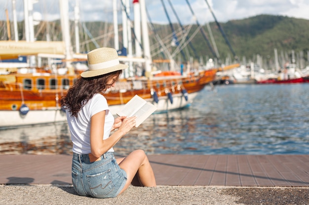 Joven mujer leyendo un libro en el puerto