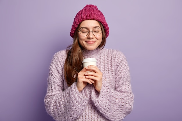 Joven mujer morena vestida con un suéter morado y sosteniendo una taza de café