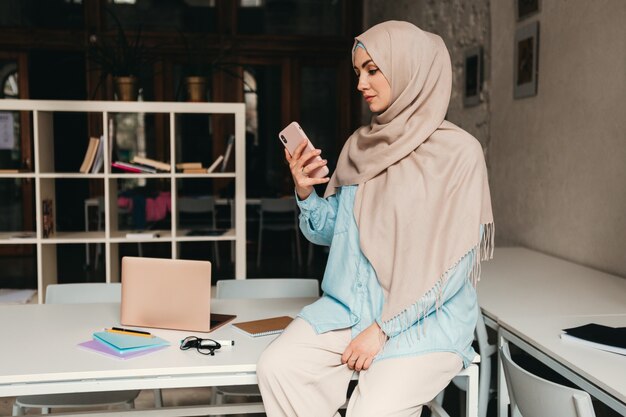 Joven mujer musulmana bastante moderna en hijab trabajando en la sala de la oficina, educación en línea