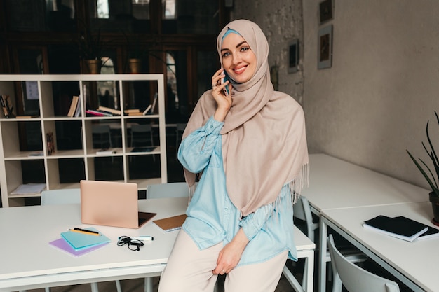 Joven mujer musulmana bastante moderna en hijab trabajando en la sala de la oficina, educación en línea