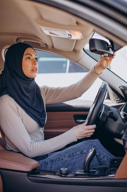 Joven mujer musulmana sentada en su coche y mirando en el espejo