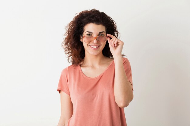 Joven mujer muy elegante con gafas, pelo rizado, sonriente, emoción positiva, feliz, aislada, camiseta rosa