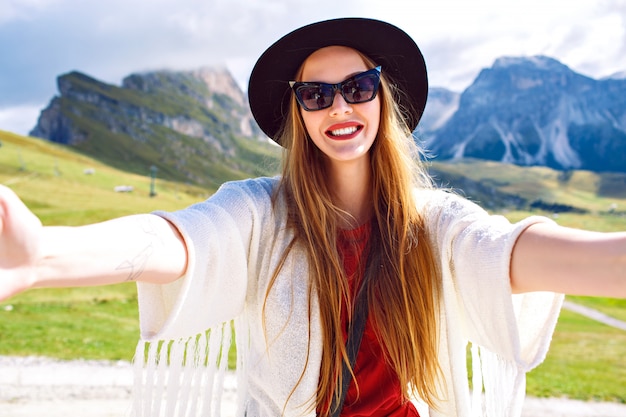 Joven mujer muy de moda haciendo selfie en montañas austriacas