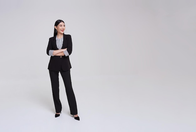 Joven mujer de negocios asiática en traje con los brazos cruzados y sonrisa en postura de pie