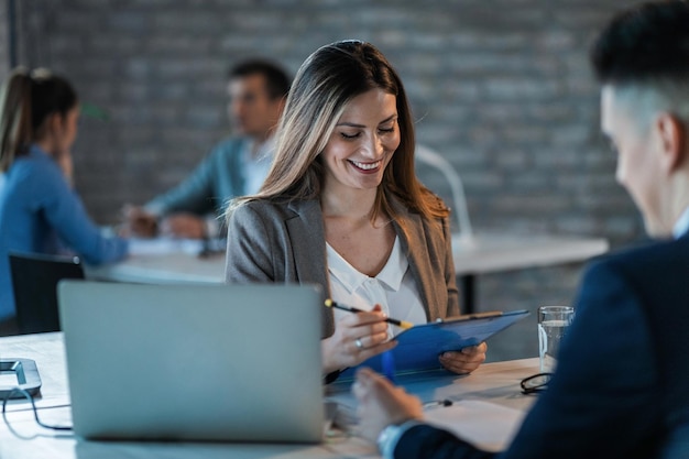 Foto gratuita joven mujer de negocios feliz leyendo informes mientras revisa el papeleo y trabaja con un colega en la oficina