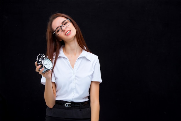 La joven mujer de negocios en gafas con reloj despertador en un espacio negro