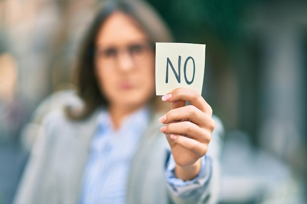 Joven mujer de negocios hispana con expresión seria sosteniendo un recordatorio sin mensaje en la ciudad