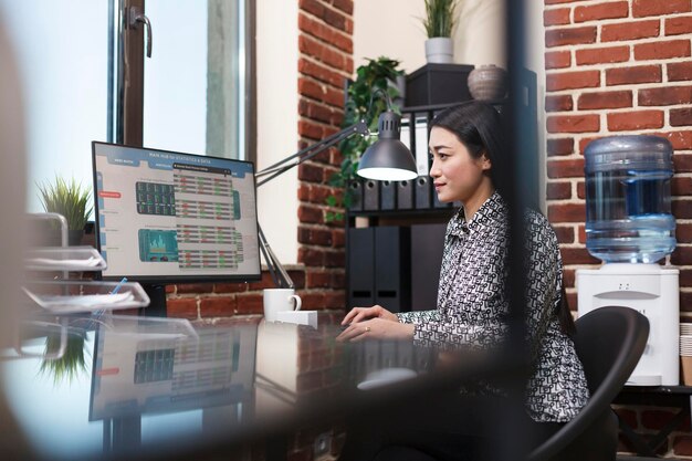 Joven mujer de negocios segura de sí misma revisando los gráficos de estado del proyecto de inicio mientras está sentada en una oficina moderna. Trabajador de oficina de la empresa de investigación de marketing que analiza las estadísticas y los datos financieros de la organización.