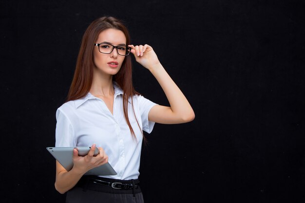 La joven mujer de negocios con tableta en pared negra