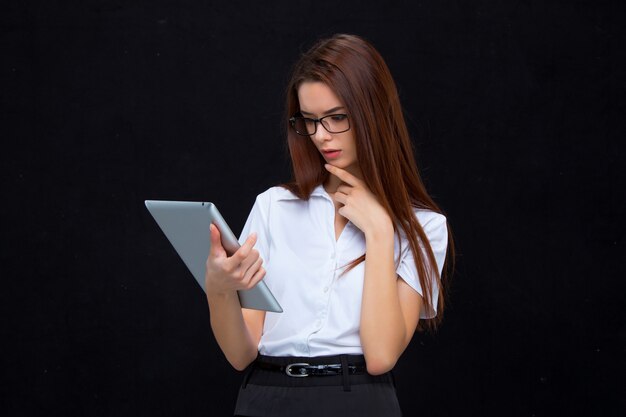 La joven mujer de negocios con tableta en pared negra