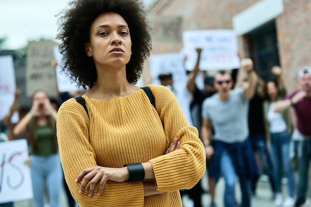 Joven mujer negra segura de sí misma con los brazos cruzados participando en una protesta por los derechos humanos