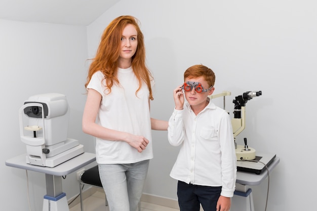 Foto gratuita joven mujer óptica mirando a la cámara mientras examina los ojos del niño paciente