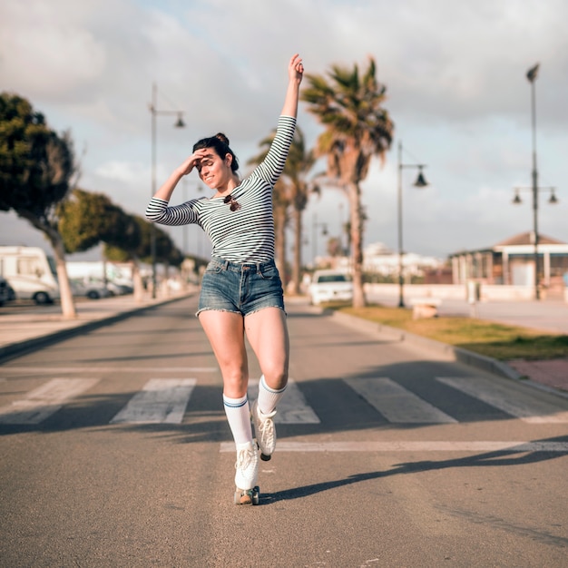 Joven mujer patinadora con su brazo levantado bailando en carretera
