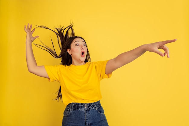 Joven mujer de pelo negro en camiseta amarilla contra la pared amarilla