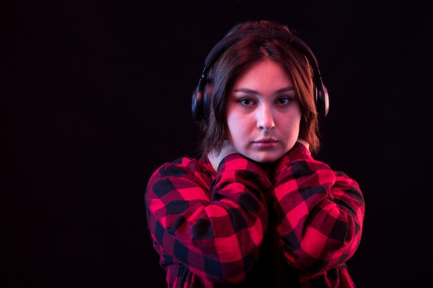 Joven mujer posando con camisa roja y negra a cuadros con auriculares