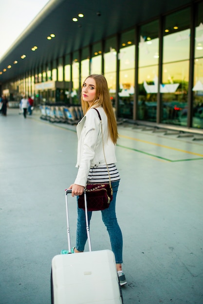 Foto gratuita joven mujer reflexiva camina con maleta blanca a lo largo del aeropuerto