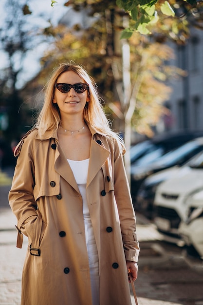 Joven mujer rubia en abrigo beige caminando en la calle