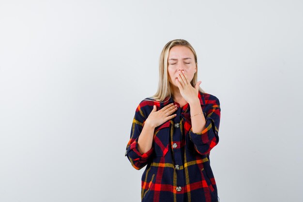 Joven mujer rubia en una camisa bostezando