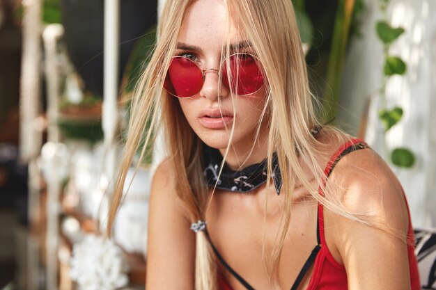 Joven mujer rubia con elegantes gafas de sol rojas, plantea interiores