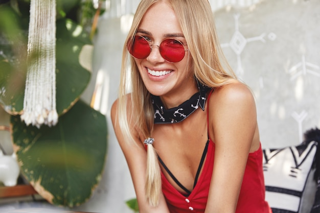 Joven mujer rubia con elegantes gafas de sol rojas, plantea interiores