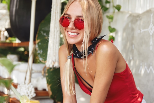 Joven mujer rubia con elegantes gafas de sol rojas, plantea interiores