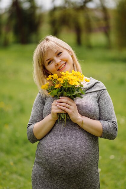 Joven mujer rubia embarazada en vestido gris, niña embarazada en primavera en un paseo, concepto de maternidad