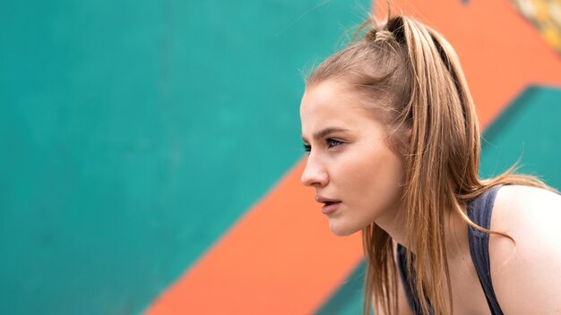 Joven mujer rubia enfocada en el entrenamiento al aire libre preparándose para comenzar a correr, fondo multicolor