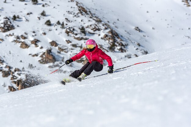 Joven mujer rubia en gafas de esquí y casco de esquí en la ladera de una montaña nevada