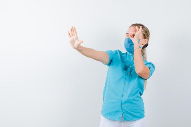 Joven mujer rubia mostrando signo de ok en el ojo mientras hace gesto de parada en ropa casual