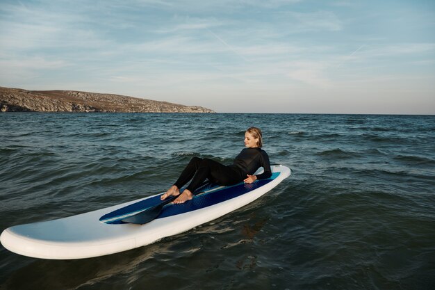 Joven mujer rubia en paddleboard en el mar