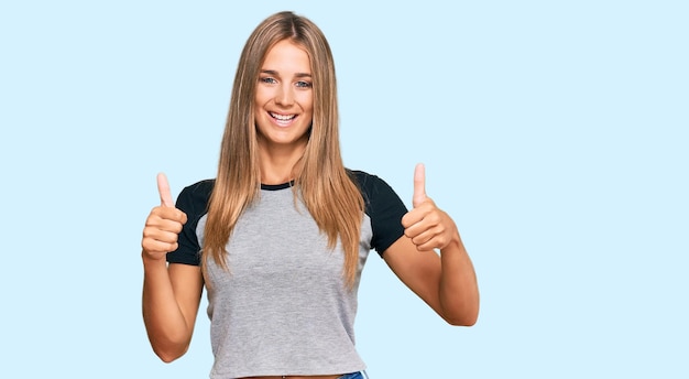 Joven mujer rubia con ropa informal signo de éxito haciendo un gesto positivo con la mano, pulgares arriba sonriendo y feliz. expresión alegre y gesto ganador.