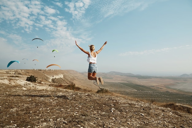 Joven mujer rubia saltando en la cima de la colina