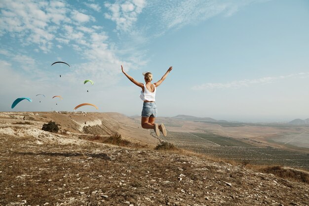 Joven mujer rubia saltando en la cima de la colina