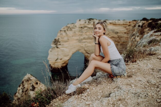 Joven mujer rubia sentada en un acantilado y disfrutar de la vista del océano