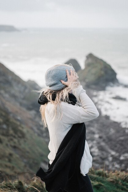 Joven mujer rubia con un sombrero divirtiéndose en la playa en un clima ventoso