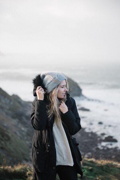 Joven mujer rubia con un sombrero divirtiéndose en la playa en un clima ventoso
