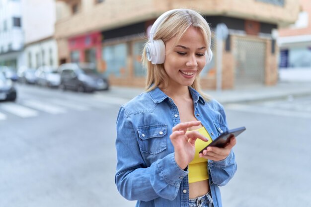 Joven mujer rubia sonriendo confiada escuchando música en la calle