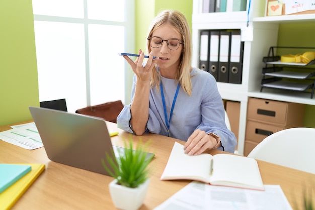 Joven mujer rubia trabajadora de negocios hablando en un teléfono inteligente leyendo un cuaderno en la oficina