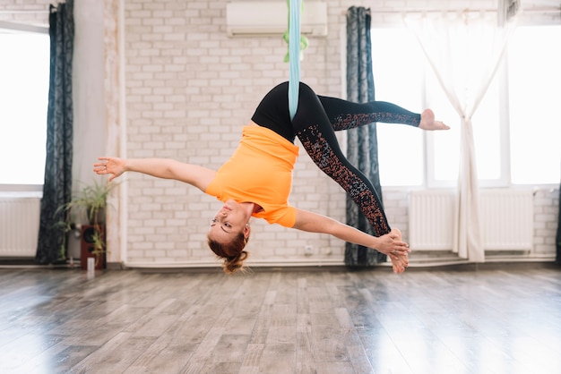 Joven mujer sana flexible haciendo yoga aérea en gimnasio