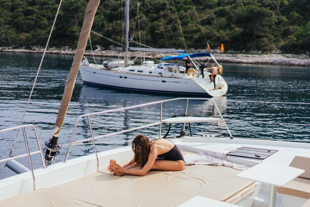 Joven mujer sana y tranquila haciendo yoga en velero velero en mar en la isla