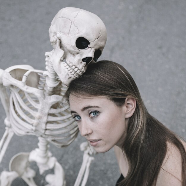 Joven mujer sentada con esqueleto y mirando a cámara