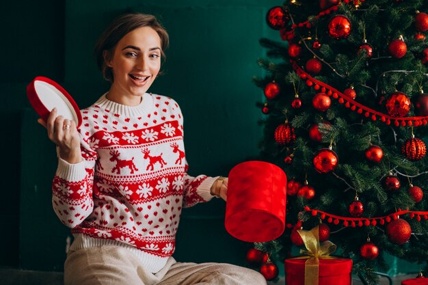 Joven mujer sentada junto al árbol de Navidad con cajas rojas